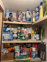 Photo showing assorted cleaning supplies on shelves including sprays, liquids, boxes with light bulbs, and utility items.
