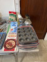 Photo showing metal coffee pots, coffee filters, sweetener, new bakeware packs, and cookbooks on a table.