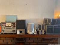 Wide shot showing Knight tube checker, Altec Lansing speaker, Harman Kardon subwoofer and satellites, and black cube bookshelf speakers on a wooden surface