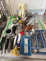 Full display of assorted cutlery, kitchen utensils, grilling tools, scissors, electric can opener, and mini spatulas in package.