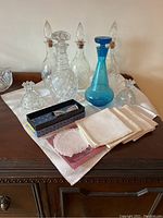 Full lot including glass decanters, candle holders, jigger, linen tea cloth and napkins arranged on wooden surface