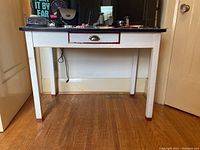 Front view of desk showing white painted wood with black tabletop and center drawer with metal cup pull handle.