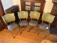 Set of four retro vinyl dining chairs placed side by side against a wall with wooden floor and radiator visible.