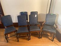 Wide shot of all six dining chairs, showing one with arms and five without, all with blue upholstery and carved wooden legs