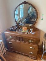 Full view of vintage wooden dresser with oval mirror attached, showing top surface with various small items.