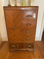 Front view of vintage wood veneer dresser with five drawers and one cabinet door, showing wood grain and carved drawer pulls.