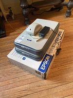 Two stacked Epson Perfection 1260 scanners on original Epson Perfection 1260 box along with power adapter and white accessory.