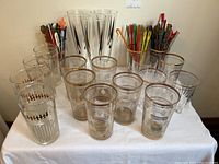 Overall view of all glassware and swizzle sticks arranged on a table with a white cloth background.