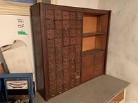Front view of wooden hardware cabinet with many small drawers on the left and shelves/drawers on the right