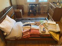 View of assorted linens including folded bedsheets, pillows, and a rolled comforter on a bed frame.