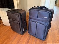 Two black fabric suitcases side by side on wood floor, showing front and part of side profile with handles and wheels.