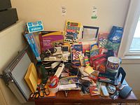 Photo of assorted office supplies on wooden table including puzzle books, scissors, envelopes, power bar, sticky notes, adhesive tape, and various small office gadgets.