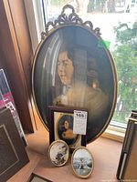 Five oval picture frames displayed on wood surface by window with outdoor snowy scene, containing vintage portraits and photos.