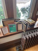 Wide view showing multiple picture frames stacked and leaned on window sill, various finishes and sizes