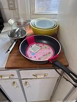 Full view of bowls, saucepan and frying pan on wooden surface by window.