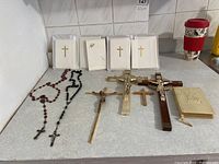 Photo showing two rosaries, three crucifixes, small crosses, condolence cards, and prayer book arranged on a white surface