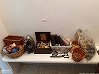 Photo showing assortment of baskets, iron, thread box, scissors, and yarn assortment on a shelf