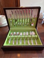 Full view of the flatware set inside wooden case with green and pink fabric lining, showing all 45 pieces arranged for 8 place settings