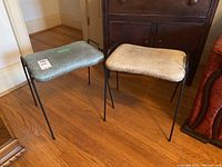Two metal stools on wood floor, positioned side-by-side, showing vinyl upholstered seats and black metal legs.