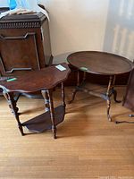Photo of oval and demi-lune wood side tables side by side on wooden flooring