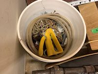 Photo of bucket containing assorted tools such as chain, tubing, wire stripper, wire brushes, and putty knife