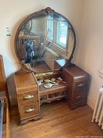 Photo of the vintage wooden vanity dresser with large ornate round mirror and vintage grooming brushes placed on top
