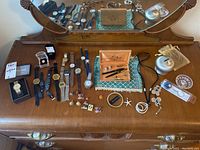 Wide view of men's wristwatches, women's jewelry, and lapel pins on wooden dresser with mirror