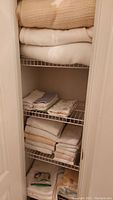 Closet shelves with folded blankets, towels, washcloths, shower curtain, and rings on lower shelf.