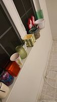 Wide side view of various glass sundae cups, vases and ceramic planters arranged along a windowsill.