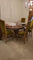 Photo showing dining table with oval dark wood top and four matching green velvet upholstered chairs in a dining room setting.