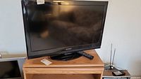 Dynex 32 inch flat-screen TV on wooden stand with remote on surface.