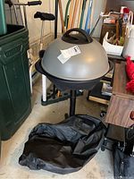 Full view of George Foreman electric grill on standby with black cover bag beneath it in garage setting.