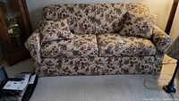 Front view of sofa bed showing tan floral upholstery and two matching pillows.