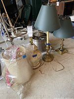 Three lamps on floor, two with green shades and brass bases, one with ceramic floral base wrapped in plastic