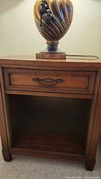 First nightstand showing wooden top surface, single drawer with decorative metal handle, and open bottom storage.