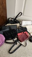 Several women's purses and bags arranged on floor, mainly black, with some white, red, and cream colors visible, in various styles including shoulder bags, clutches, and wallets.