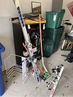 Shows K2 skis, wooden baseball bat, hockey stick, racor metal rack, and some ski boots with storage bins in background