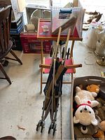 Photo showing metal umbrella stroller with small plastic wheels, child's wooden desk and chair, plastic bin filled with plush toys and paper dolls in a garage setting.