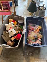 Two bins side by side: one with assorted stuffed animals, the other with vintage dolls and doll accessories in plastic bags.