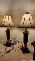 Pair of tulip-shaped table lamps positioned side by side on carpeted floor with cords visible and fabric bell-shaped shades