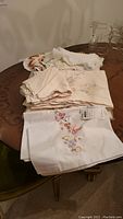 Overview of assorted linens stacked on a wooden table with some lace and embroidered details visible