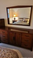 Matching wooden wall mirror with rectangular frame in medium brown finish hanging above the dresser