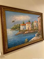 Front view of the framed wall art depicting a coastal village scene with water and sky