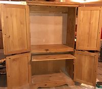 Front view of wooden armoire with all four doors open showing pull-out tray and lower compartment.