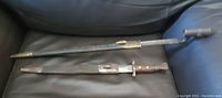Two bayonets laid on black leather surface, showing wood handles, metal blades and scabbards