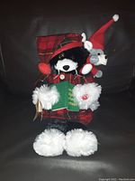 Stuffed black and white cat in red plaid nightcap and gown holding a plush mouse and green book with embroidered Christmas text.