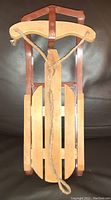Front view of decorative sled showing wood slat seat, curved wooden handle, and attached rope for pulling