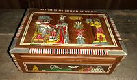 Closed wooden box showing detailed Egyptian artwork on lid and sides, colorful and bordered by striped edges.