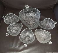 Complete set of one large clear glass strawberry-shaped bowl and five smaller matching bowls displayed on a dark leather surface.