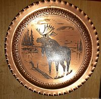 Copper-toned metal hanging plate with a raised border and engraved moose and nature scene